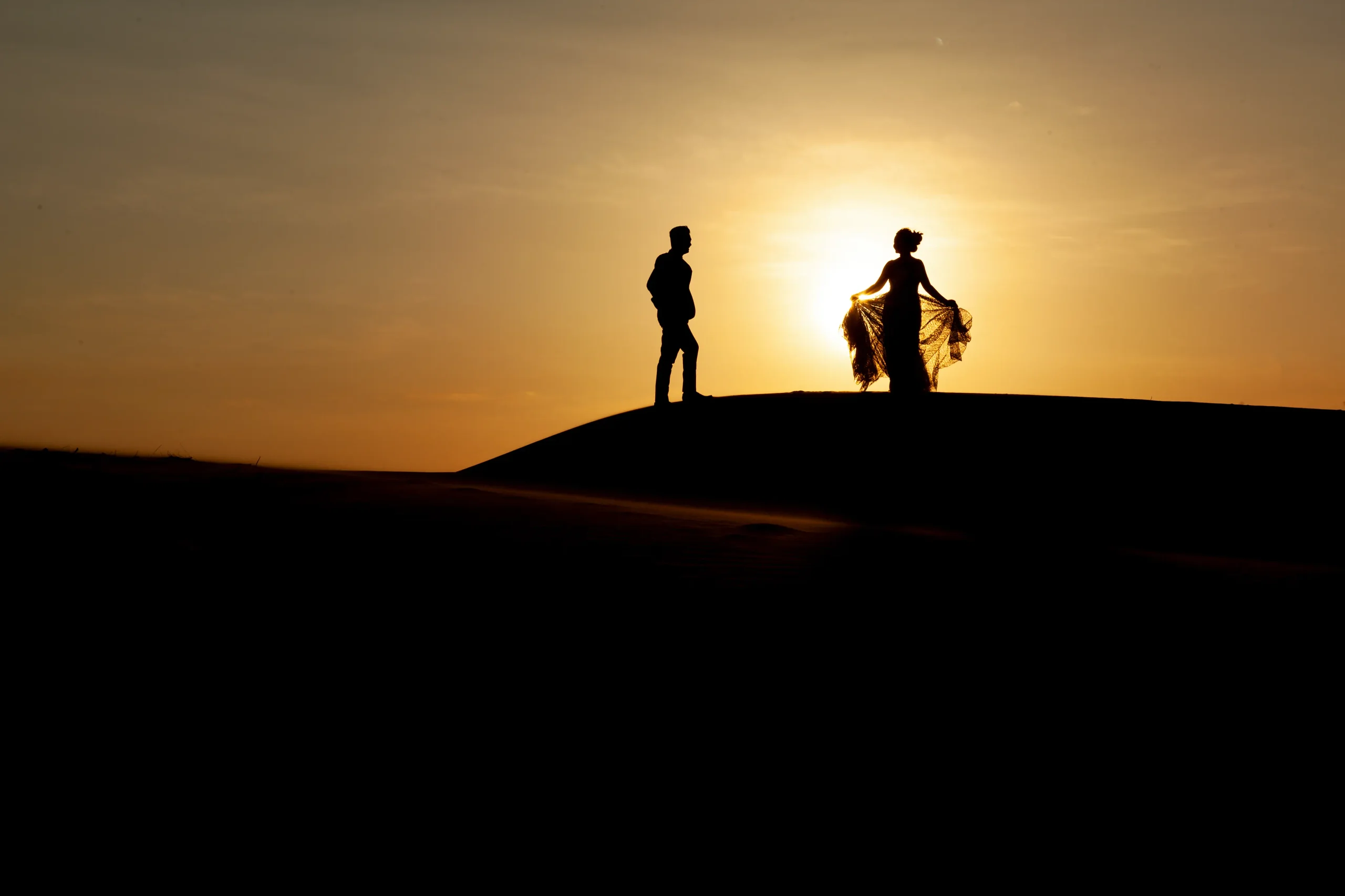 Silhouettes d’un couple sur une dune au coucher du soleil